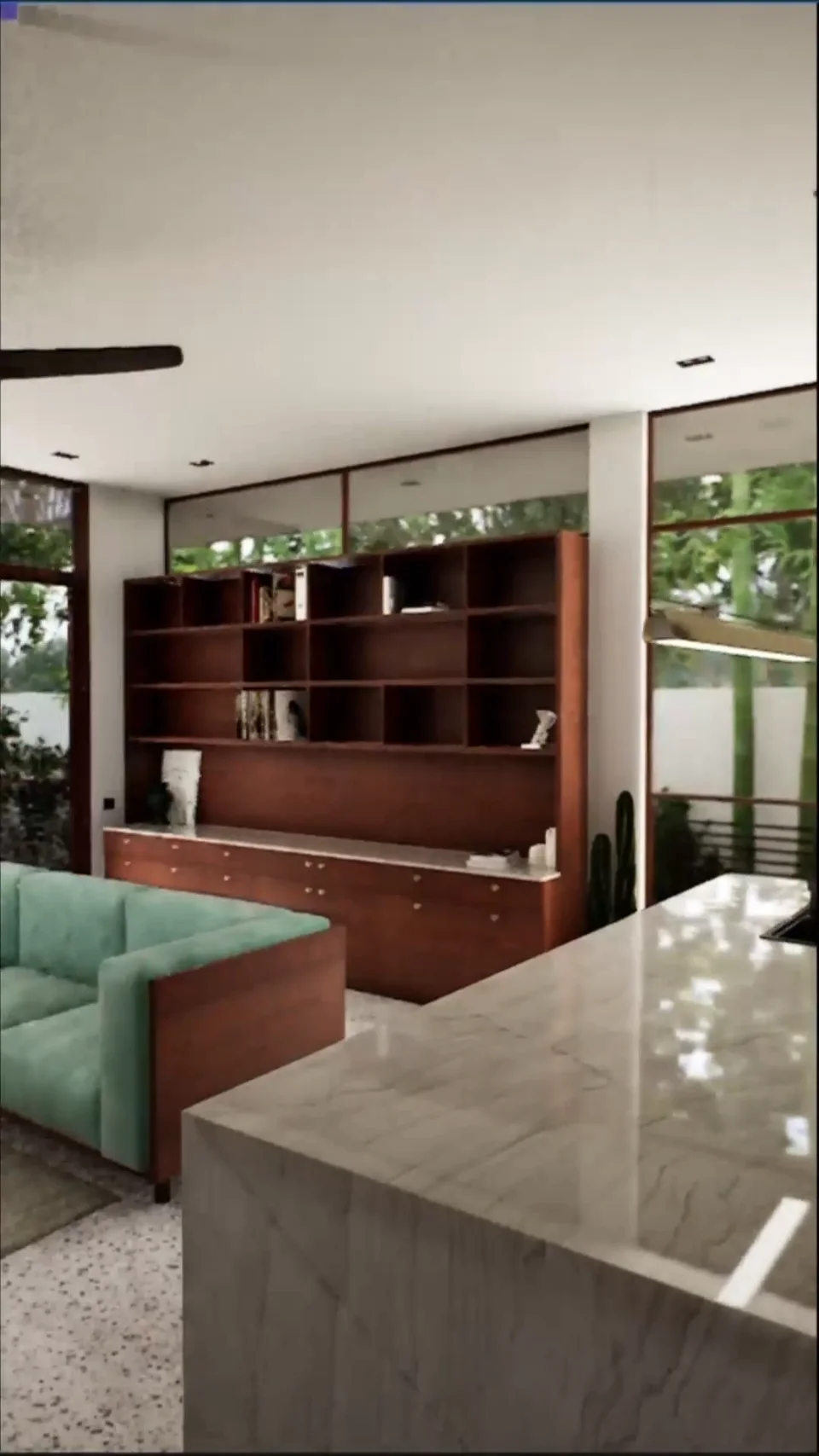 Green sofa beside dark wood shelving, pale counters and garden-facing windows
